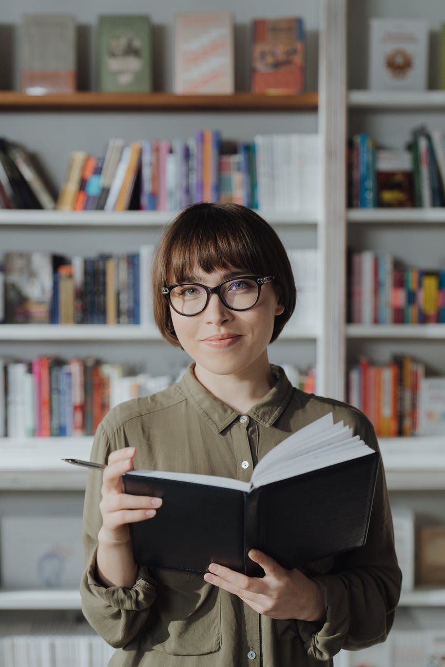 woman in green button up shirt wearing black framed eyeglasses reading book